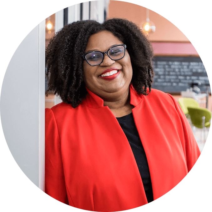 Emily Brown CEO and Co-Founder of Attane Health leans against a wall in a red shirt.